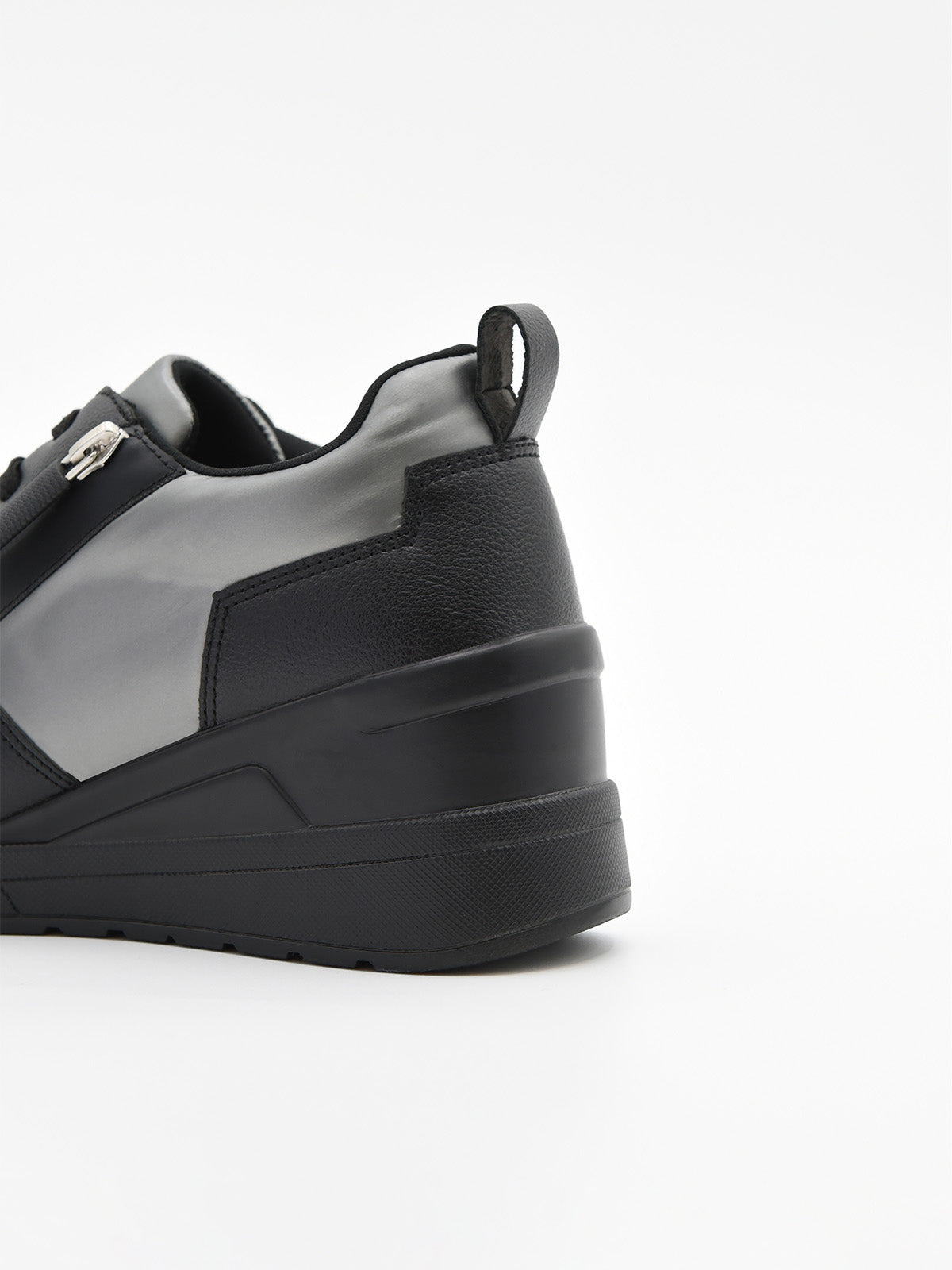 Zapatilla deportiva de mujer negra con cuña interna, detalles en gris metalizado, cordones, logo metálico y suela de plataforma ligera.