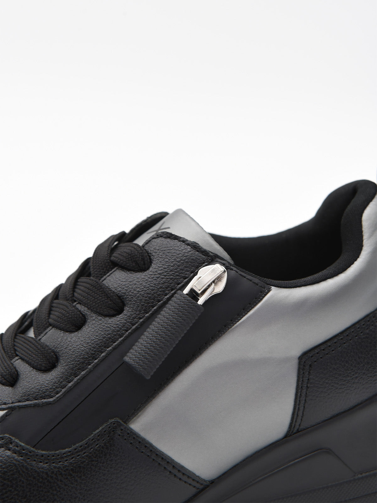Zapatilla deportiva de mujer negra con cuña interna, detalles en gris metalizado, cordones, logo metálico y suela de plataforma ligera.